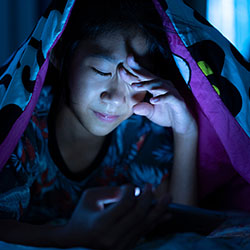 Girl using mobile phone on dark bed in the bedroom, eye strain tension